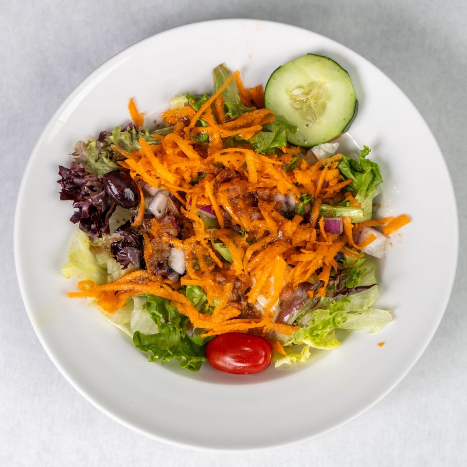 Fresh garden salad with mixed greens, shredded carrots, red onion, cucumber, and a cherry tomato.