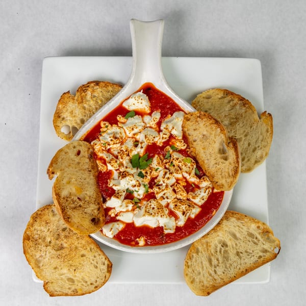 Baked ricotta cheese in tomato sauce, garnished with parsley and served with toasted bread.