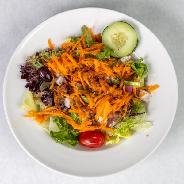 Abbondanza Cucina's house salad with mixed greens, shredded carrots, olives, onions, and a cherry tomato.