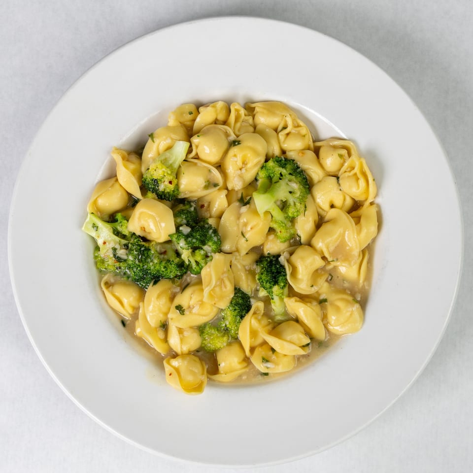 Abbondanza Cucina's tortellini with broccoli and garlic sauce, served in a white bowl.