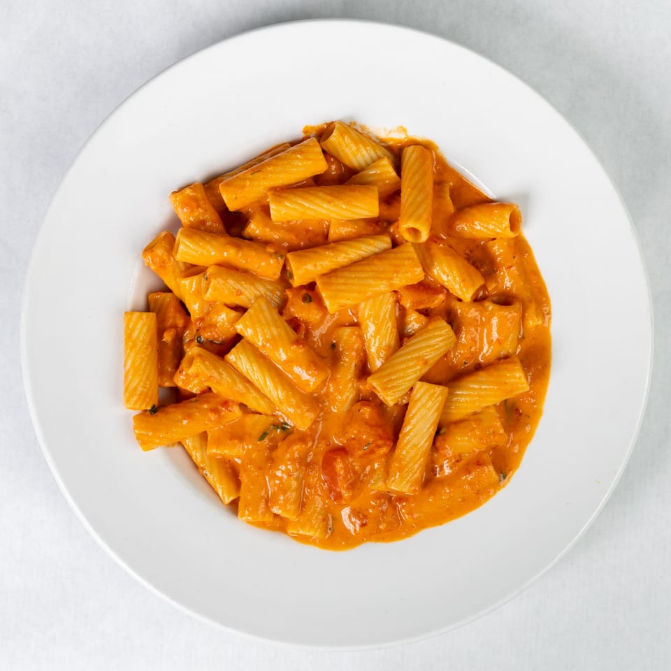 A white plate filled with rigatoni pasta in a creamy orange tomato sauce.