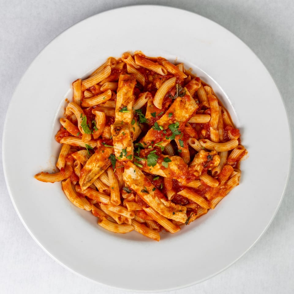 Penne pasta with chicken and red sauce, garnished with fresh parsley on a white plate.