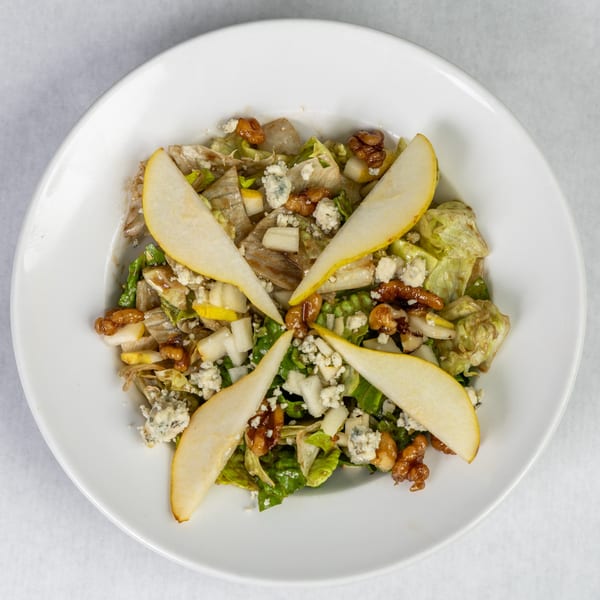 Overhead view of a salad with lettuce, pear slices, walnuts, and crumbled blue cheese in a white bowl.