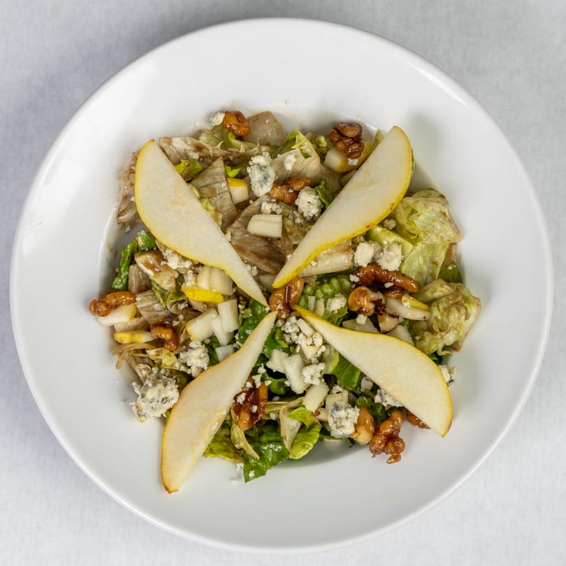 Overhead view of a salad with lettuce, pear slices, walnuts, and crumbled blue cheese in a white bowl.